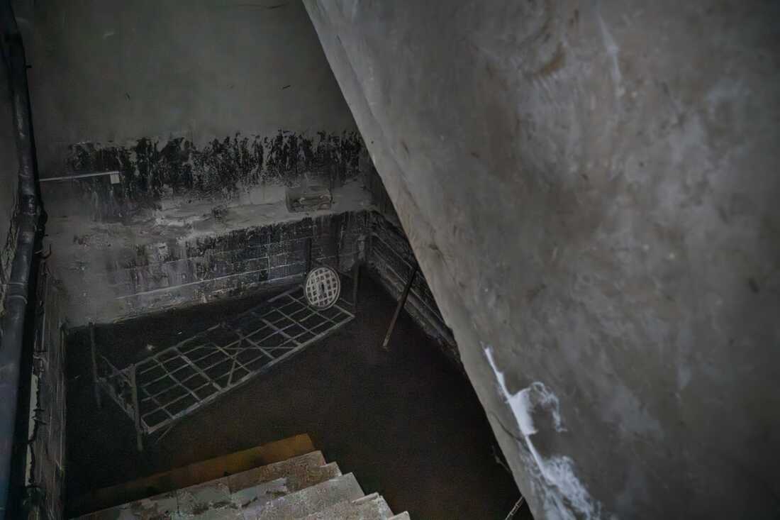 A bed frame sits in a dark room with a brown liquid covering the floor. Moustafa says its a pit of acid where detainees where thrown to die.