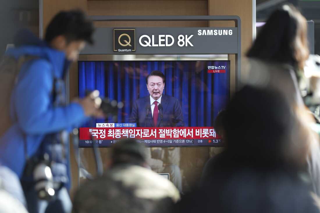 People watch a TV screen showing the live broadcast of South Korean President Yoon Suk Yeol's announcement at the Seoul Railway Station in Seoul, South Korea, on Saturday.