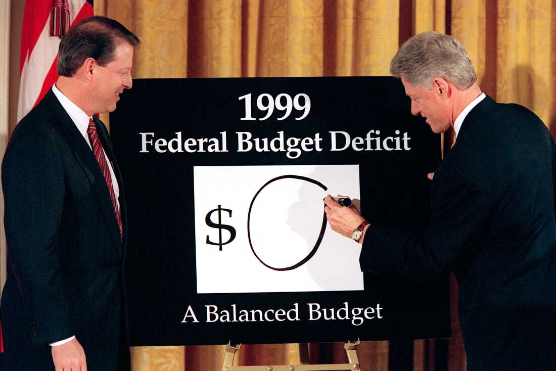 Vice President Al Gore (left) looks on as President Bill Clinton (right) places an "0" on the board showing what the federal deficit will be after unveiling his balanced budget plan for 1999.