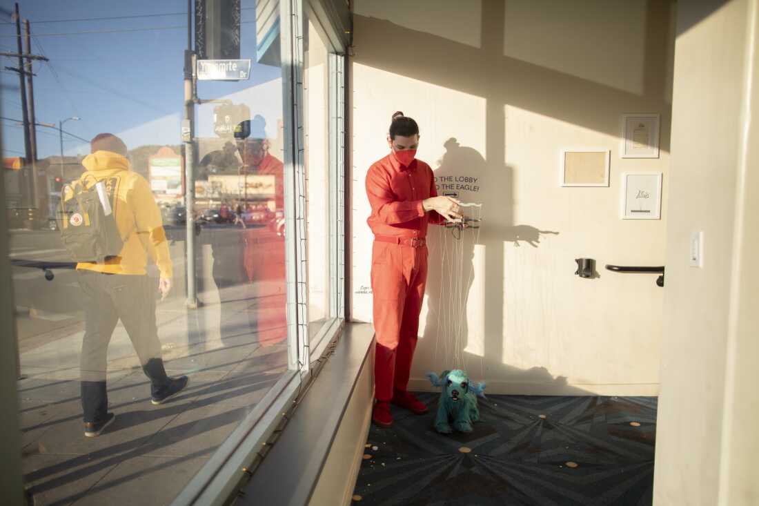 Diego Montoya, dressed in all red, shows off a blue dog marionette puppet.