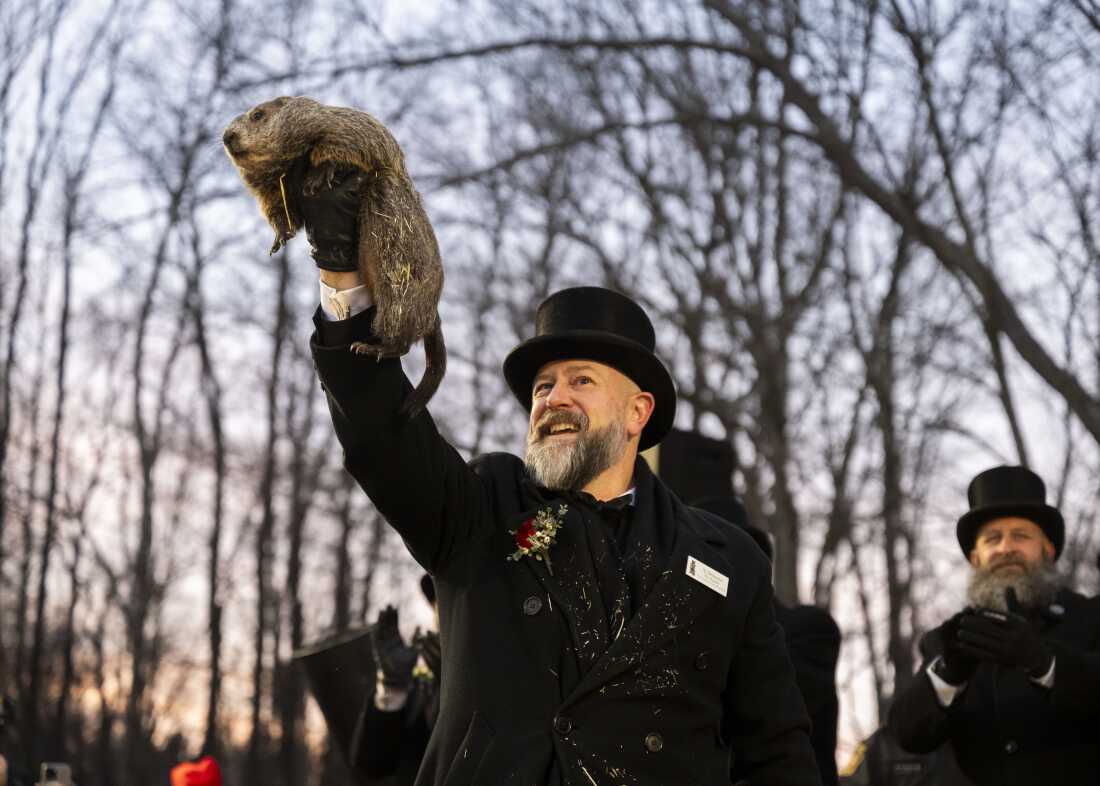 Punxsutawney Phil is held in the air by a man with a top hat.
