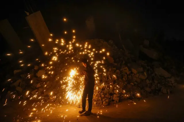 فتى فلسطيني يشعل الألعاب النارية بالقرب من أنقاض مبنى خلال احتفاله باليوم الأول من شهر رمضان في مخيم البريج للاجئين في وسط قطاع غزة في الأول من مارس 2025