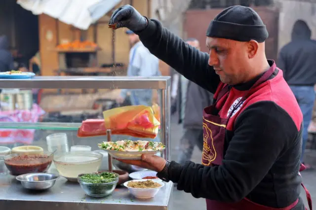 بائع يرش التوابل على طبق من الحمص من كشكه في سوق الزاوية القديم بمدينة غزة في اليوم الأول من شهر رمضان المبارك في الأول من مارس 2025