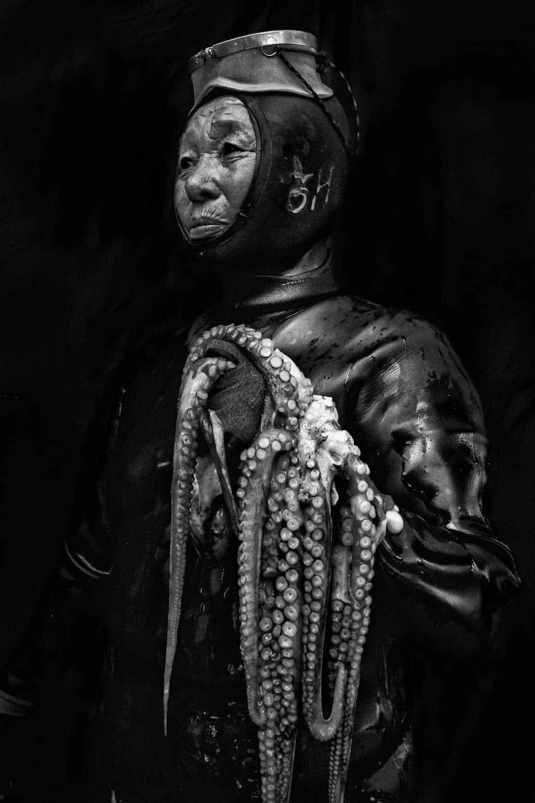 Soon-ja Hong of Seongsan comes out of the water holding an octopus. She explains that she and her fellow Haenyeo set traps to catch octopuses which come in a variety of shapes and sizes. Today she was lucky to catch this large specimen. Now 69, she is at the peak of her career, It has taken Soon-ja many years to build up her endurance and fine-tune the hunting techniques that enable her to dive most efficiently. But even the most experienced divers must follow the strict rules imposed by the fishing cooperatives including diving cycles that allow the women to work seven days on and eight days off in order to recuperate. Jeju island, known for its characteristic basalt volcanic rock, sits off South Korea. It is the home of the renowned Haenyeo or women of the sea who free dive off the black shores of Jeju harvesting delicacies from the sea. Wearing thin rubber suits and old fashioned goggles, this aging group of women are celebrated as a national treasure and inscribed on the UNESCO list of Intangible Cultural Heritage, but the tradition is slowly fading as fewer women choose this extremely hazardous profession. Today, the majority of Haenyeo are over the age of 50 and many are well over 70. In a society obsessed with education, the future of this physically arduous activity would appear bleak, and yet… Efforts by the government and local communities to preserve and promote this ecological and sustainable lifestyle have brought renewed interest from young people disillusioned with urban life and eager to return to their roots. It is perhaps a renaissance.