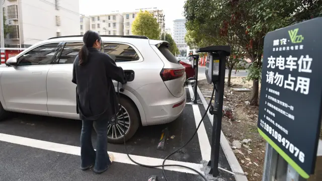 امرأة تستخدم شاحن لتعبئة بطارية سيارتها في مدينة في الصين