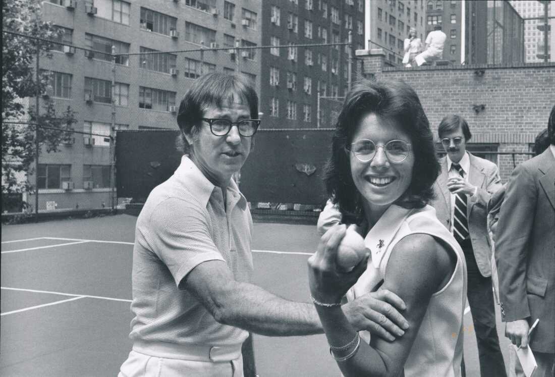 In this black-and-white photo, Billie Jean King stands with Bobby Riggs on a tennis court at a press event for the 1973 "Battle of the Sexes."