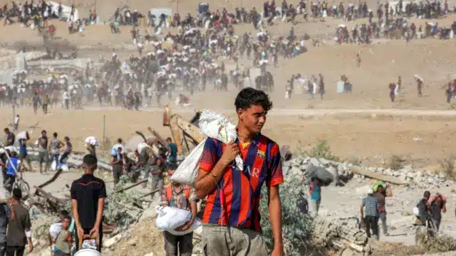 يسير الناس حاملين أكياساً من المساعدات الإنسانية التي تلقوها في مركز توزيع تديره مؤسسة غزة الإنسانية (GHF)، المدعومة من الولايات المتحدة وإسرائيل، أثناء عبورهم ما يُسمى "ممر نتساريم" في وسط قطاع غزة، في 22 أغسطس/آب 2025.
