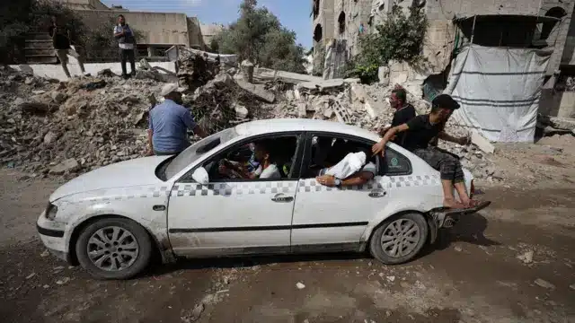 سيارة أجرة متضررة محملة بالمدنيين تمر عبر شوارع مدينة غزة، إثر غارات جوية إسرائيلية استهدفت الأحياء السكنية، في 21 أغسطس/آب 2025.