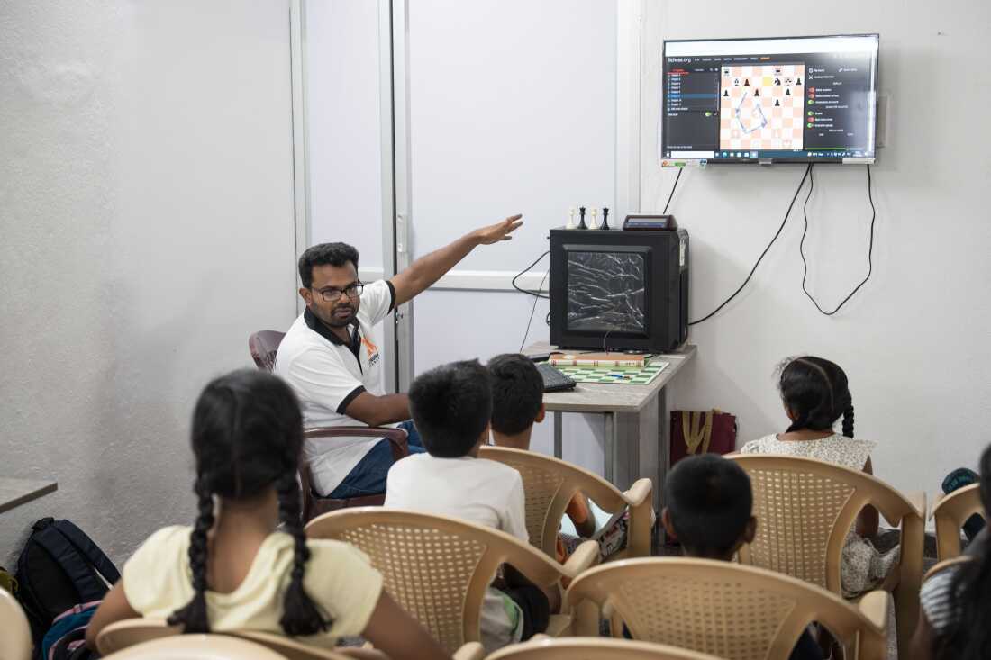 Venkatesan Enumalai conducts a chess class using the online platform Lichess.org, pointing to a monitor as he explains a position to his students.
