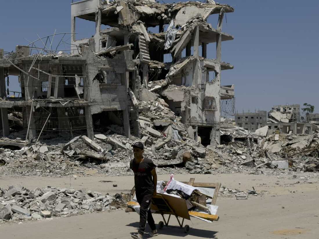 A man lugs items in a makeshift wagon in front of buildings that were bombed out by Israeli strikes in northern Gaza City, Aug. 26.