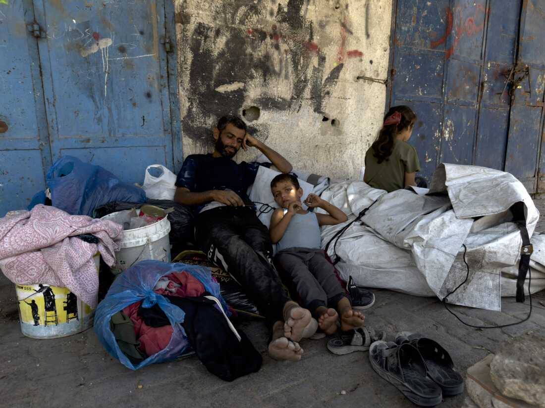A Palestinian man rests with his children and few belongings on the sidewalk in the Sheikh Radwan neighborhood of Gaza City after fleeing on foot an Israeli assault on his neighborhood further north, on Aug. 26.