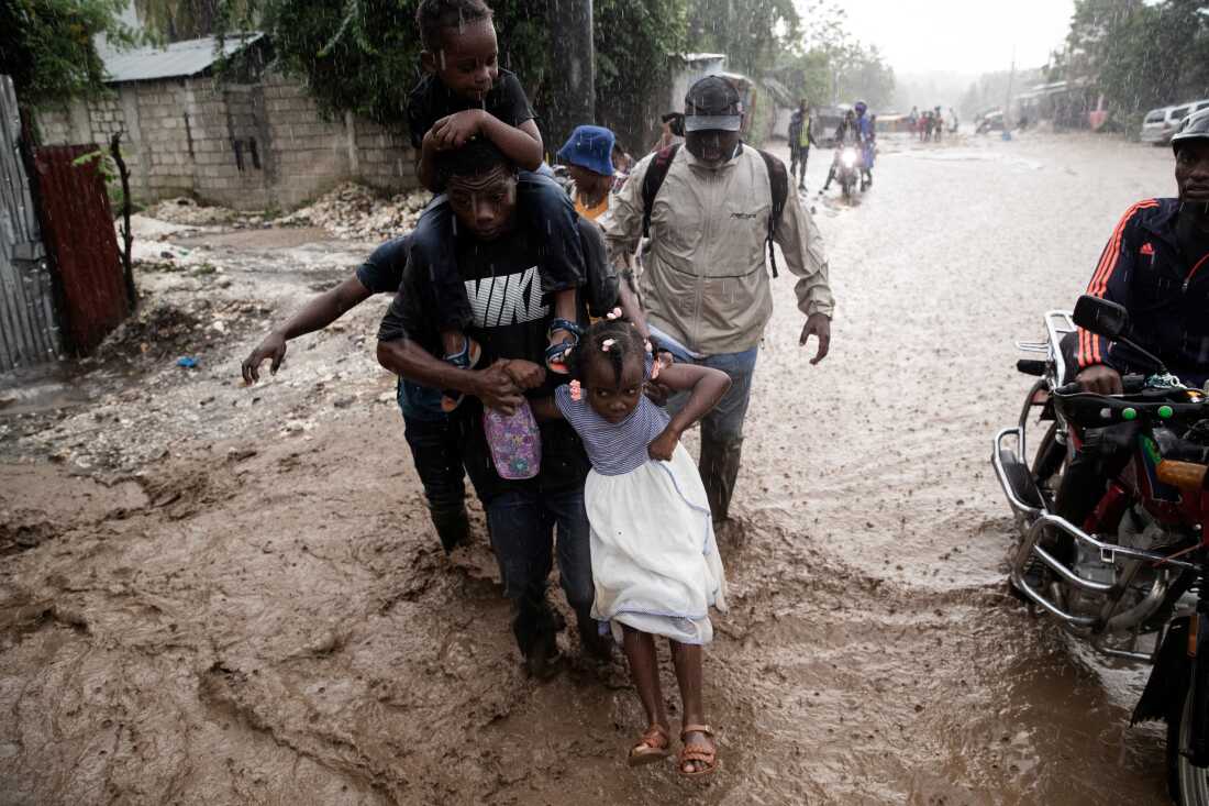 People walk through a flooded street following Hurricane Melissa in Petit-Goave, Haiti on October 30, 2025. The storm, a devastating Category 5 with sustained winds of 185 mph, killed dozens across the Caribbean.