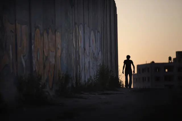 رجل يسير على طول جدار الفصل الإسرائيلي عند حاجز قلنديا في 24 أغسطس/آب 2011 في الضفة الغربية المحتلة