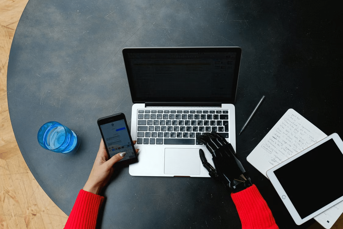 Person using a laptop and smartphone with a prosthetic hand